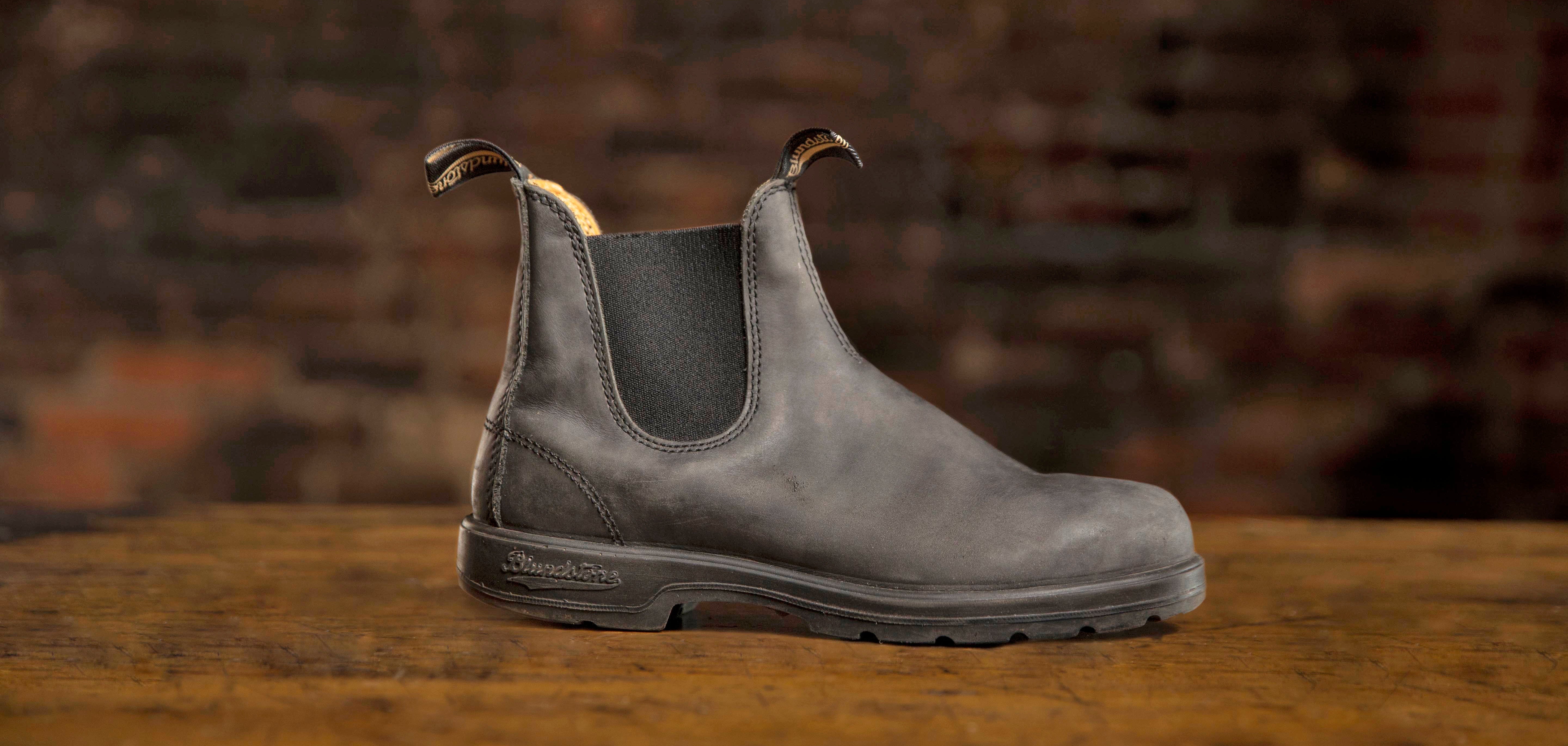 Gray Chelsea boot on a wooden surface with a brick wall background